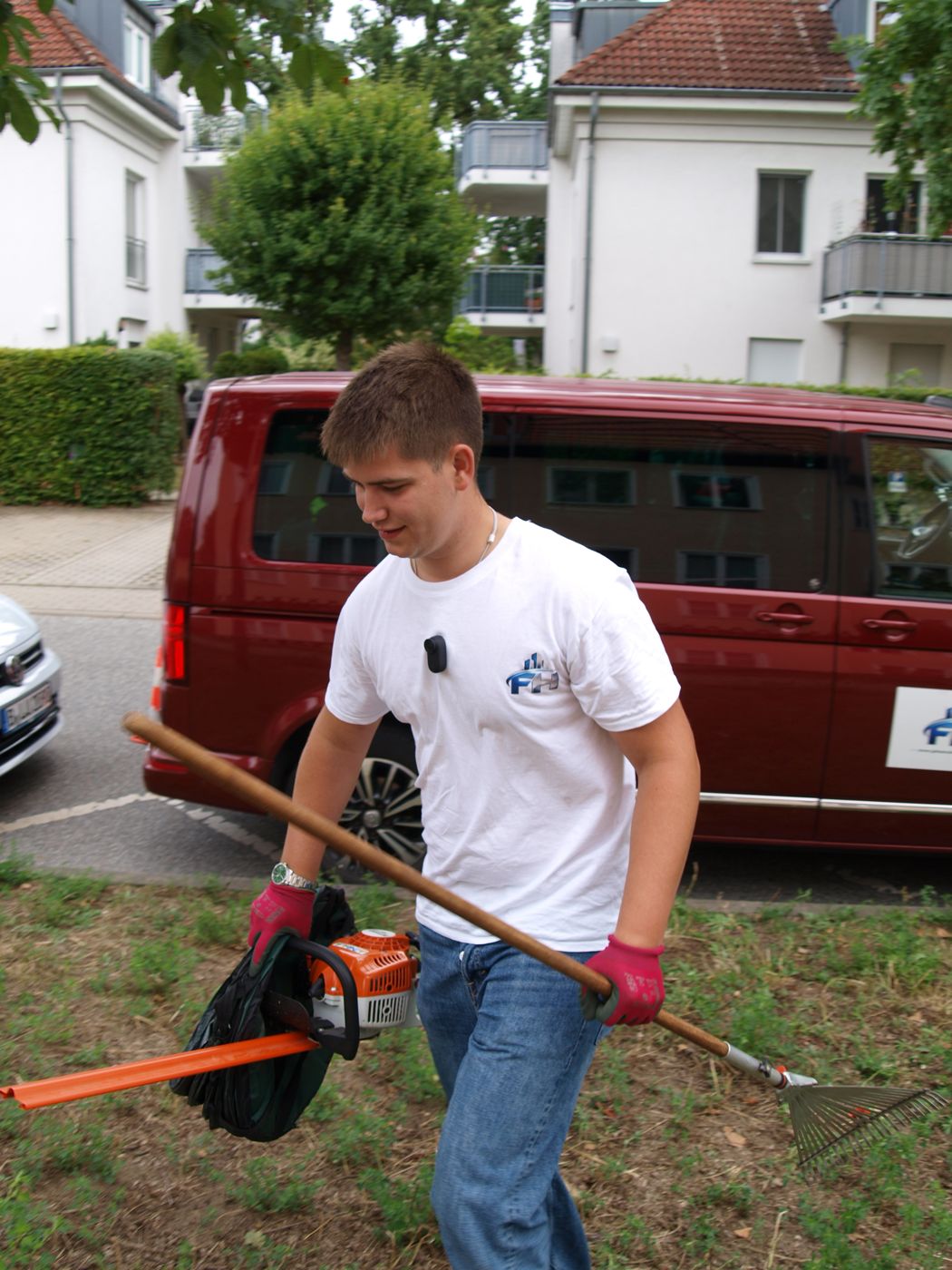 Florentin Hohenstein mit Heckenschere und Laubrechen vor dem Transporter